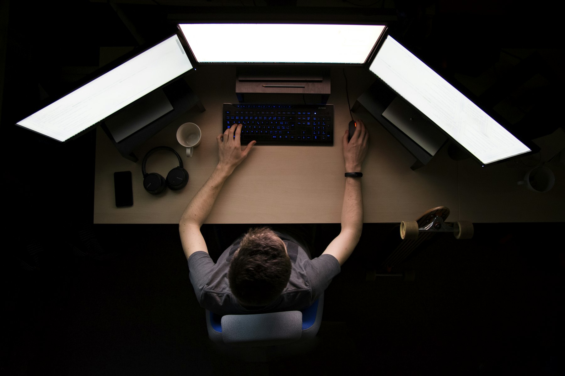 A person working across several monitors in a dark room